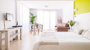 A modern hotel room with a large bed, a desk with a chair, a dining table with chairs, and a small seating area with a chair and a table. - Apartamentos Dunas Club (La Oliva)