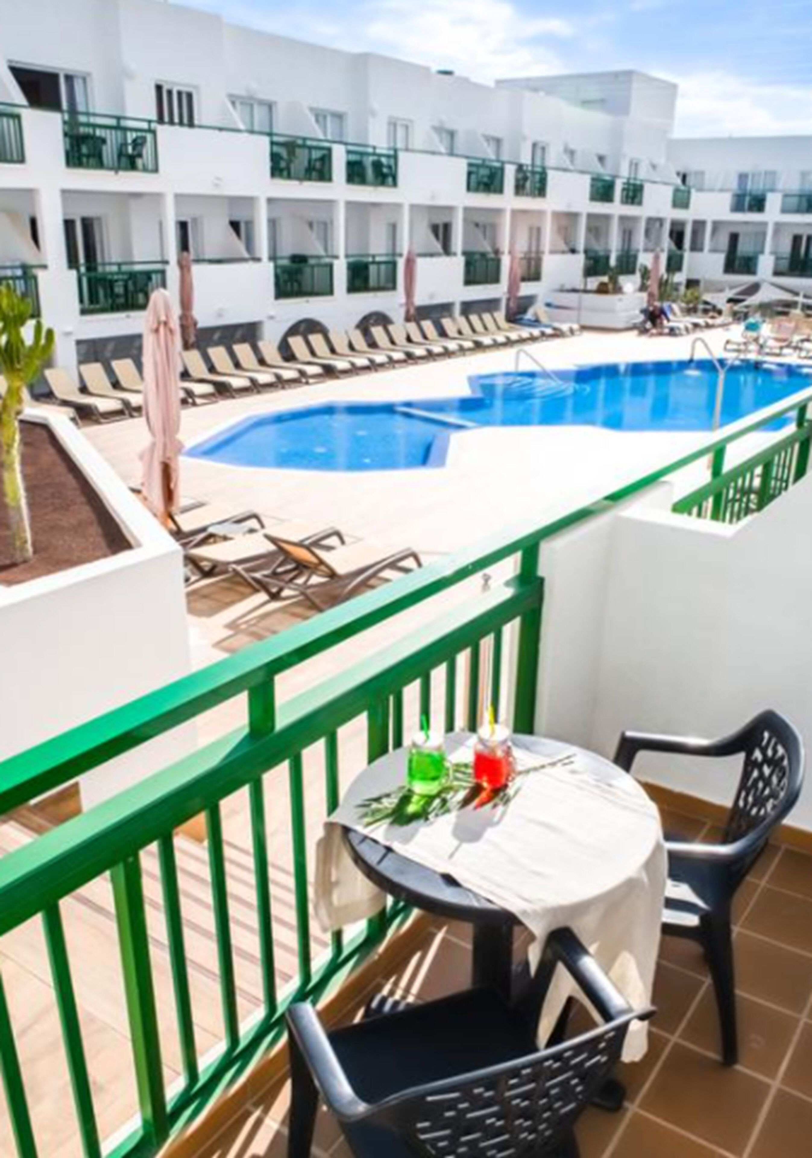 Área da piscina com espreguiçadeiras e uma mesa, cercada por um edifício branco com varandas.