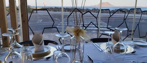 A table set for dining with a view of the ocean and a mountain in the background.