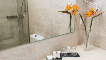 A bathroom with a white sink, a glass shower enclosure, a mirror, and a vase with flowers.