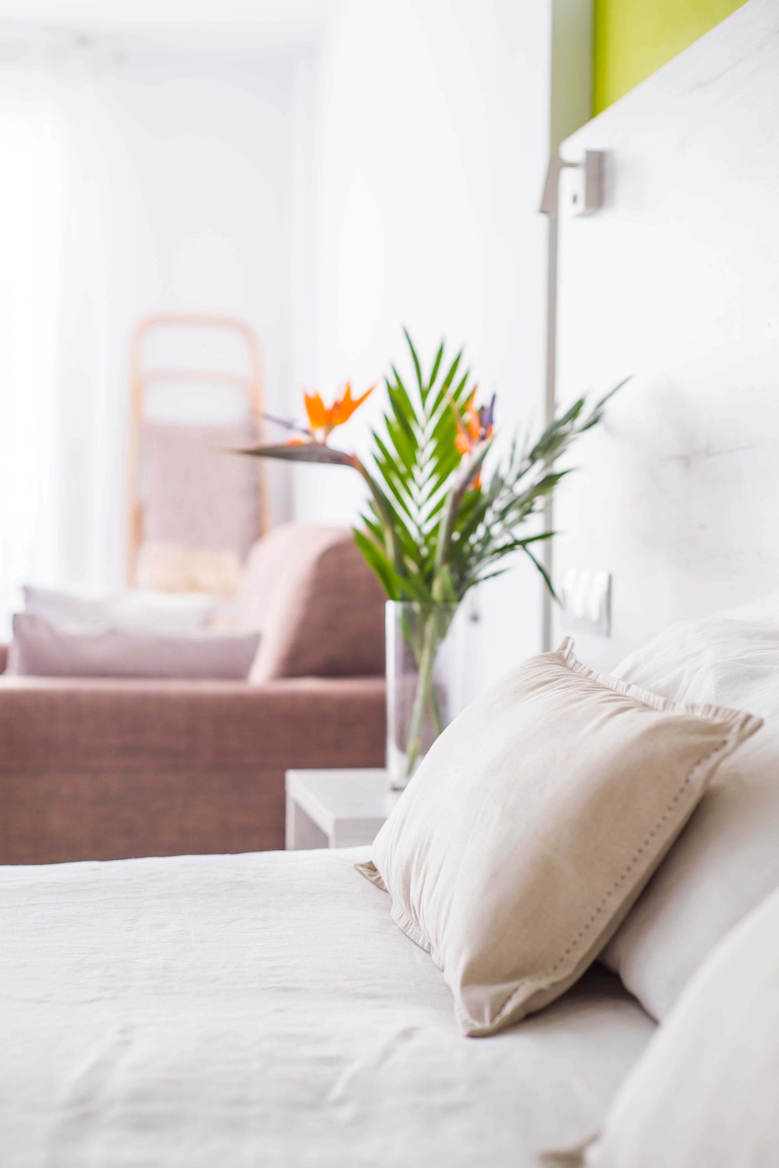 Ein ordentlich eingerichtetes Schlafzimmer mit einem Bett, Kissen, einem Nachttisch und einer Pflanze.