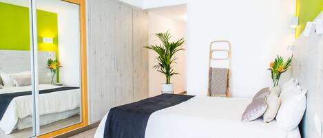 A modern bedroom with a large bed, a mirror, a potted plant, and a wooden wardrobe.