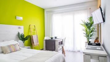 Una habitación de hotel con cama, escritorio, silla, televisor y ventana con cortinas.