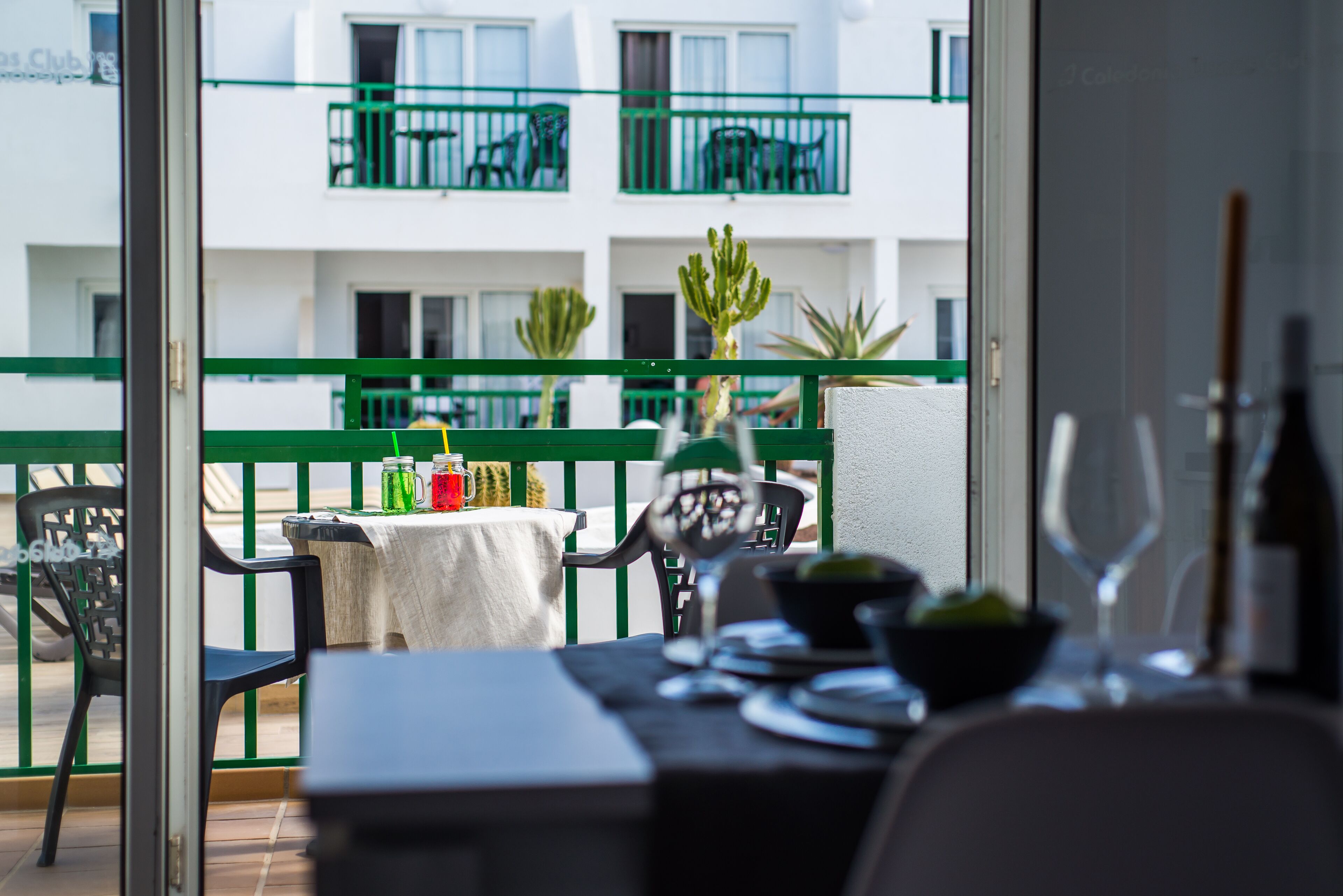 A balcony with a table set for dining, chairs, and potted plants.