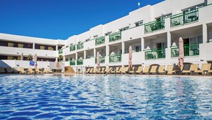 A hotel with a swimming pool, multiple balconies with green railings, and sun loungers. - Apartamentos Dunas Club (La Oliva)