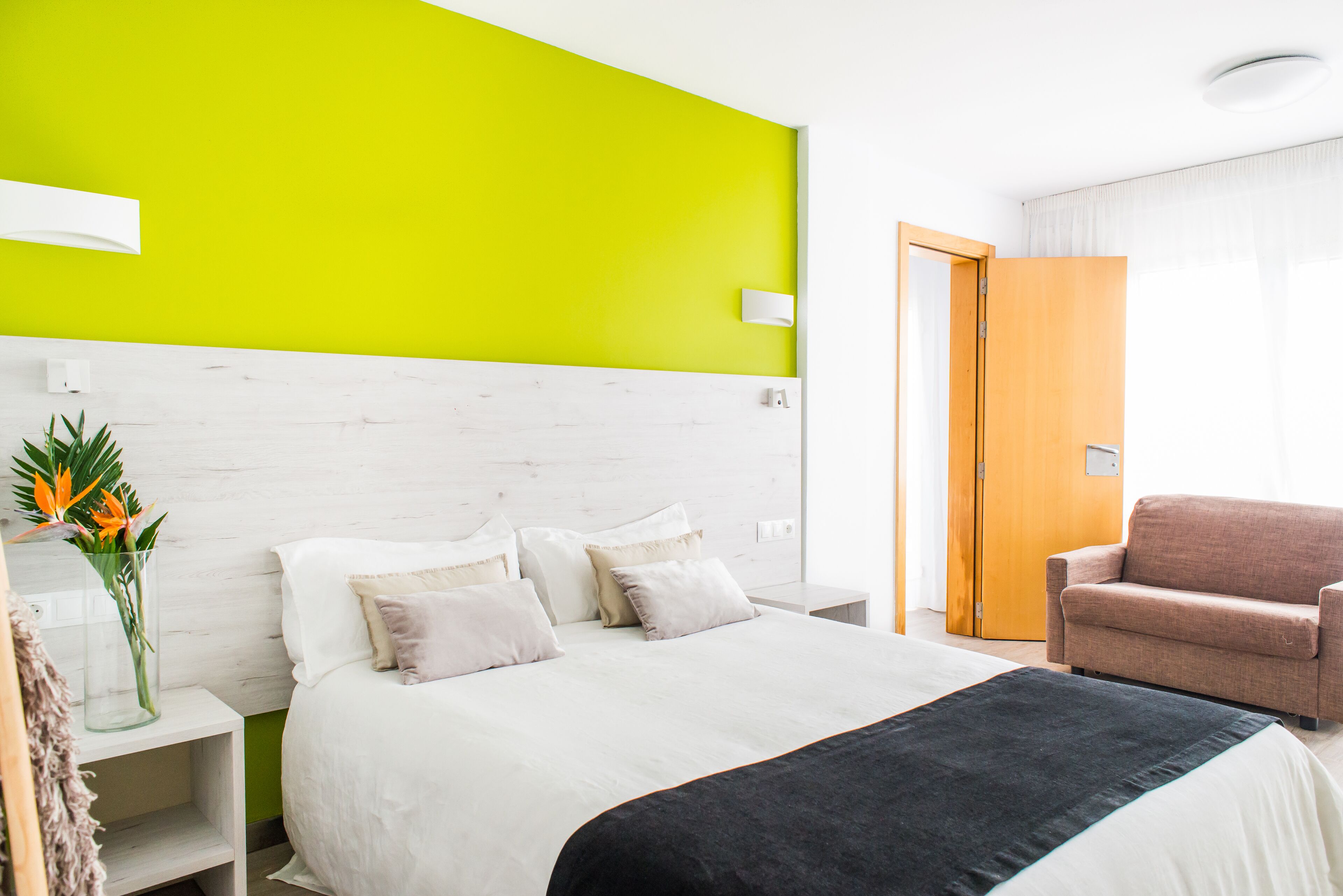 A hotel room with a bed, a nightstand, a chair, and a bright green accent wall.