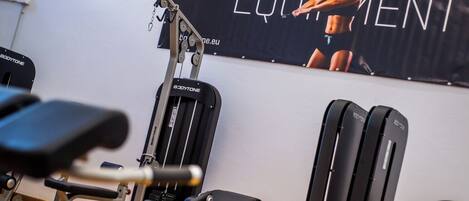 Une salle de sport équipée de divers appareils d’entraînement, notamment un banc de développé couché, une machine à câbles et un support à squats.