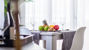 A dining area with a table set for two, featuring a fruit platter, two wine glasses, and a bottle of wine. - Apartamentos Dunas Club (La Oliva)