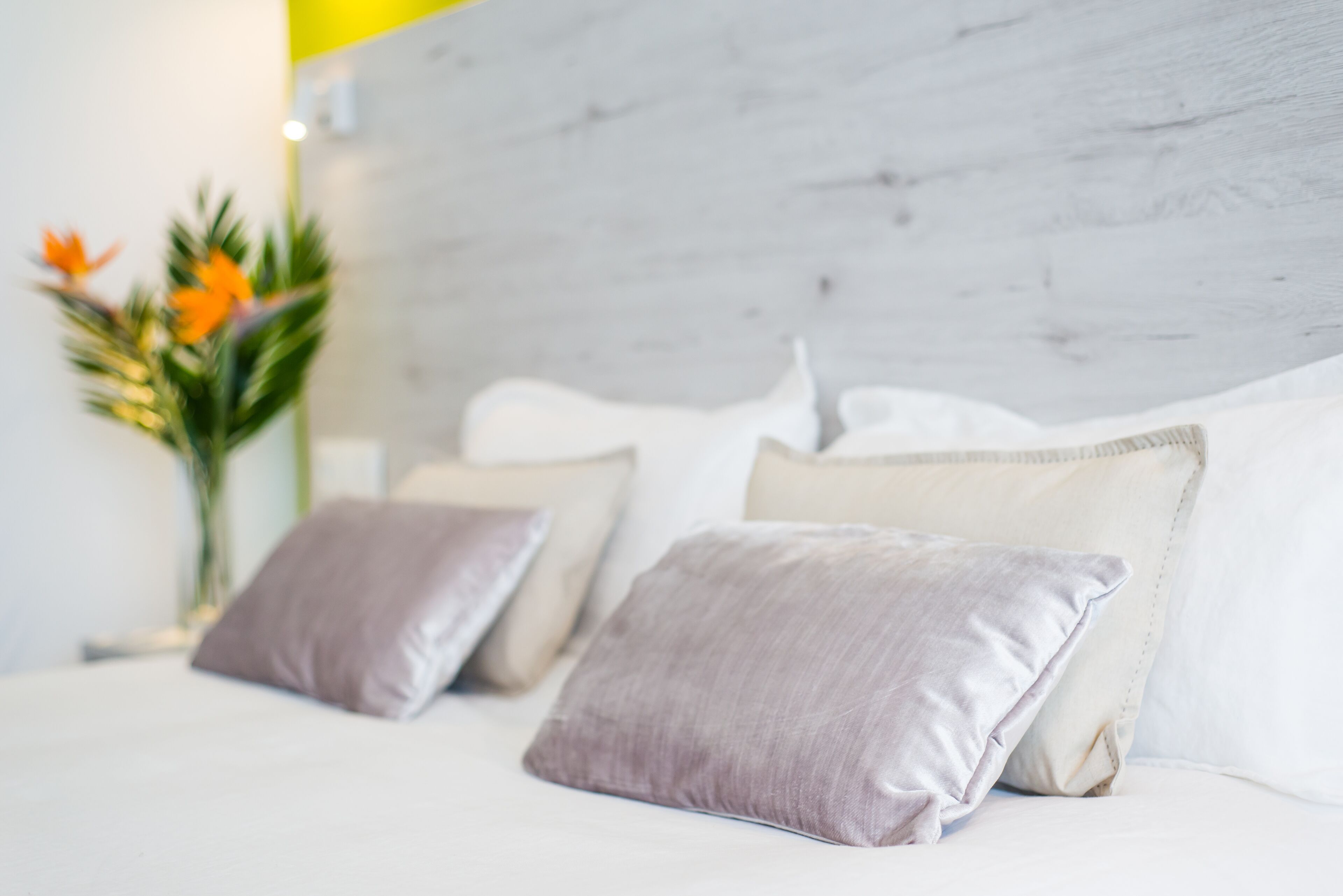 Ein Bett mit weißer Bettwäsche, zwei Kissen, einem Holz-Kopfteil und einer Vase mit Blumen.