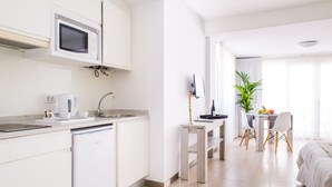 A modern, well-lit hotel room with a kitchenette, a dining area, and a bed. - Apartamentos Dunas Club (La Oliva)