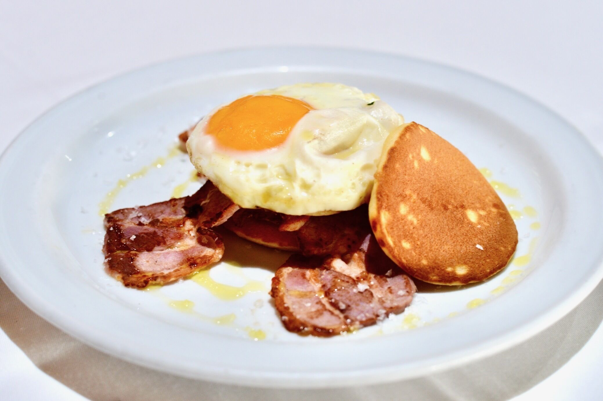Une assiette avec un œuf au plat, du bacon et des crêpes.