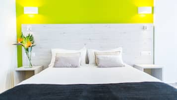 Habitación de hotel con una cama, dos mesitas de noche, una lámpara de noche, un jarrón con flores y una pared verde brillante.