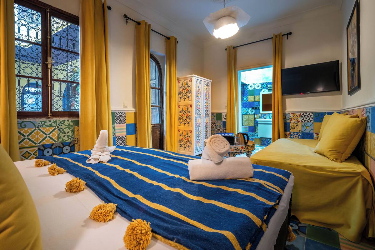 A hotel room with a bed, a TV, a cabinet, and a view of the outside.