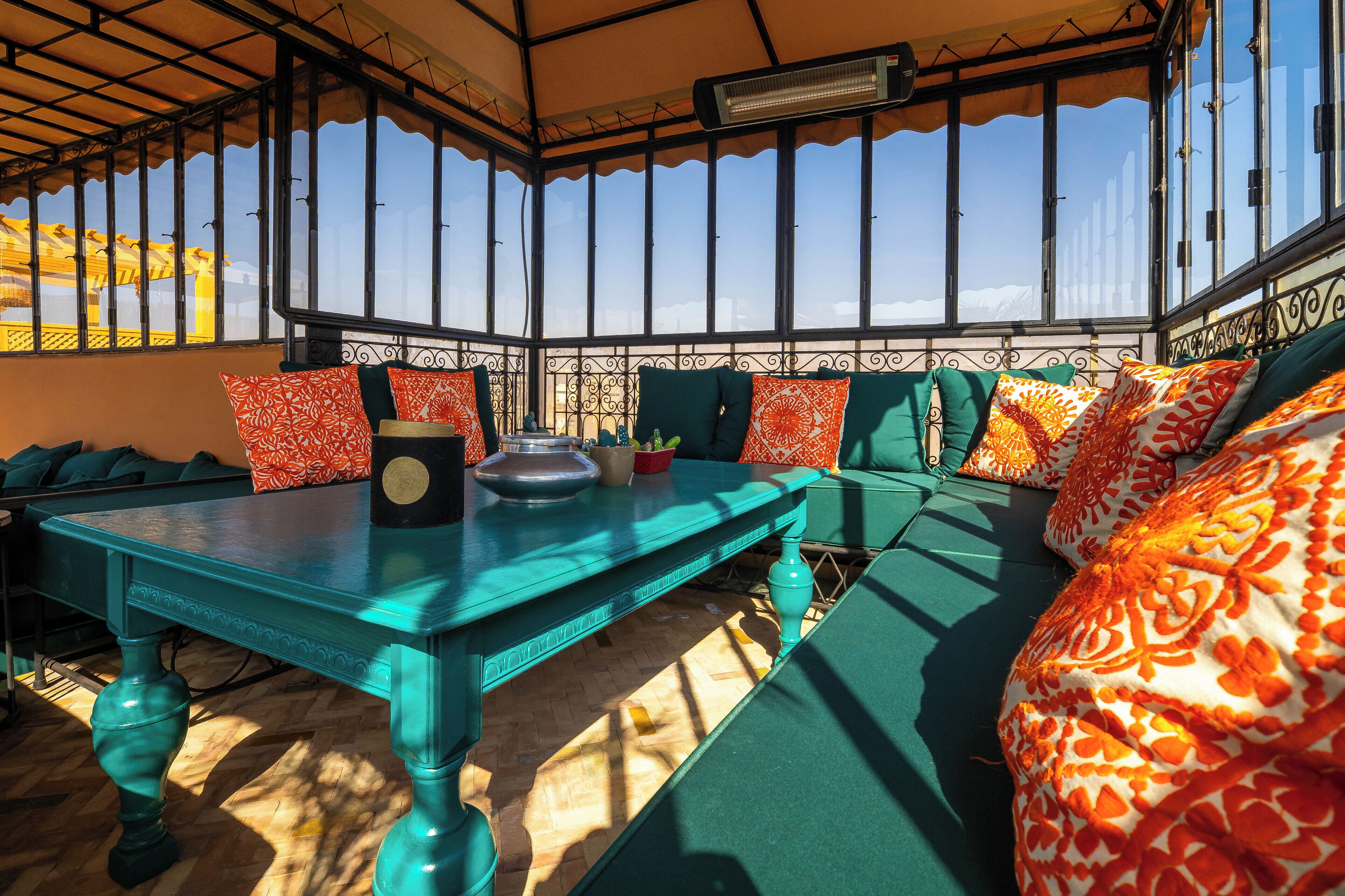 A sunlit room with a large table, green cushioned seating, and patterned cushions.