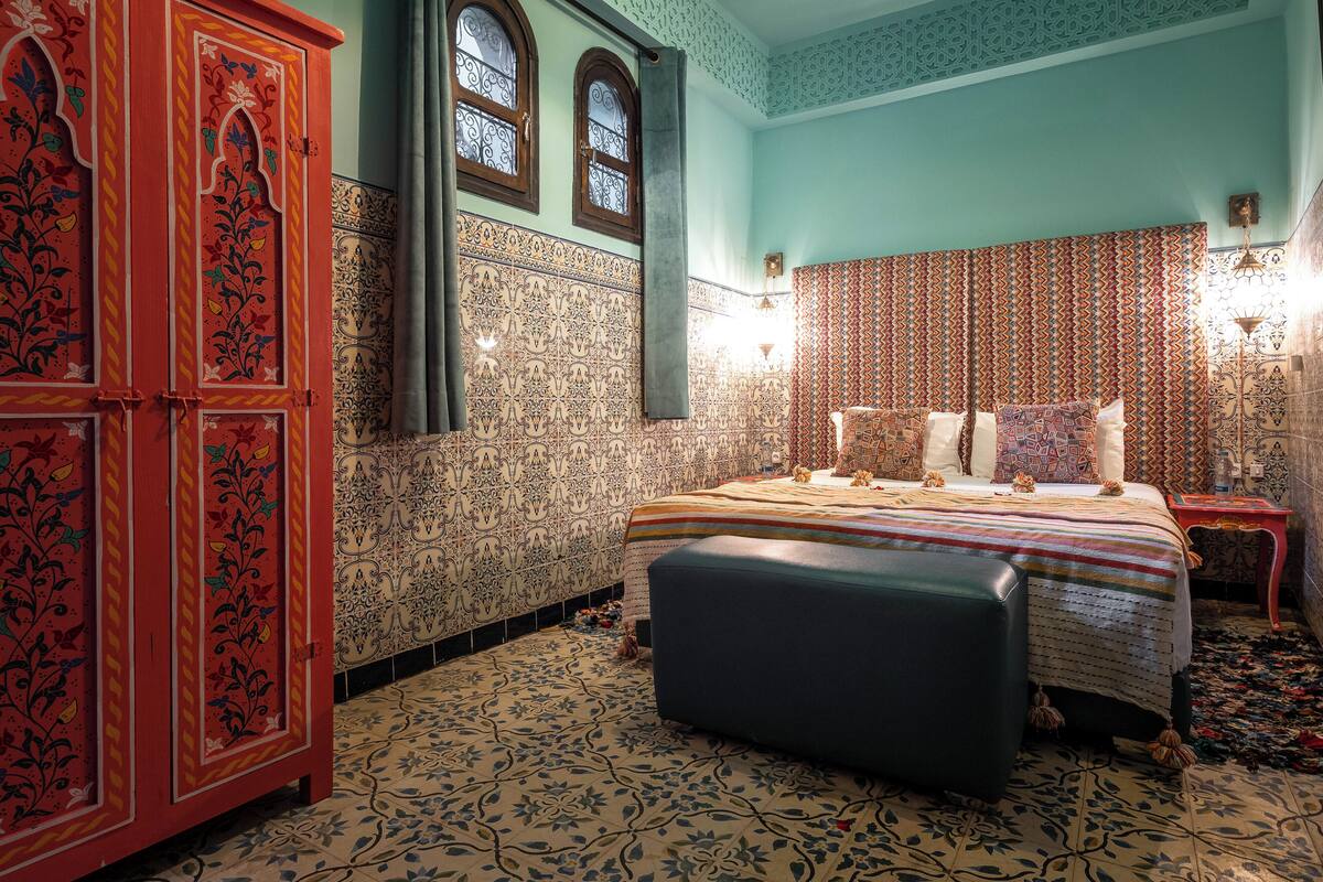 A room with a bed, a cabinet, patterned walls, and a tiled floor.