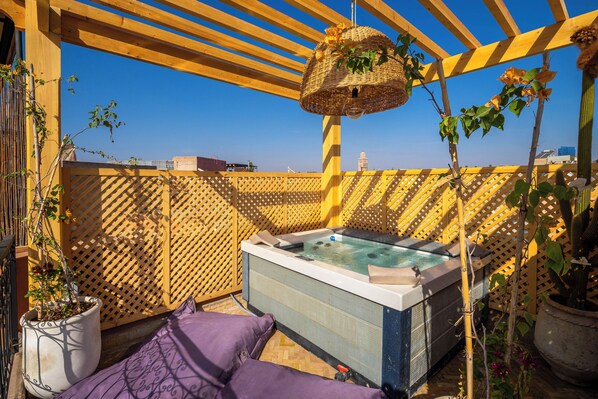 A rooftop patio with a hot tub, wooden pergola, and potted plants.