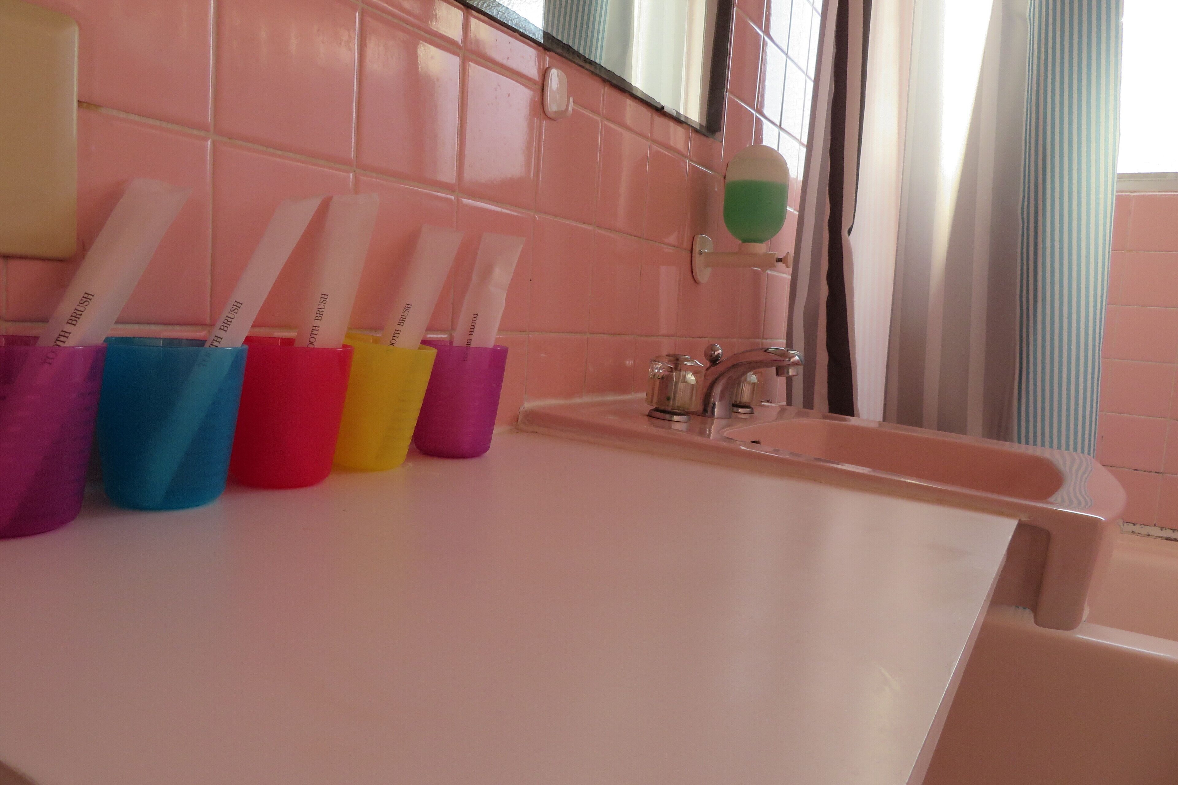 Une salle de bain avec des carreaux roses, un lavabo et des porte-brosses à dents de différentes couleurs.