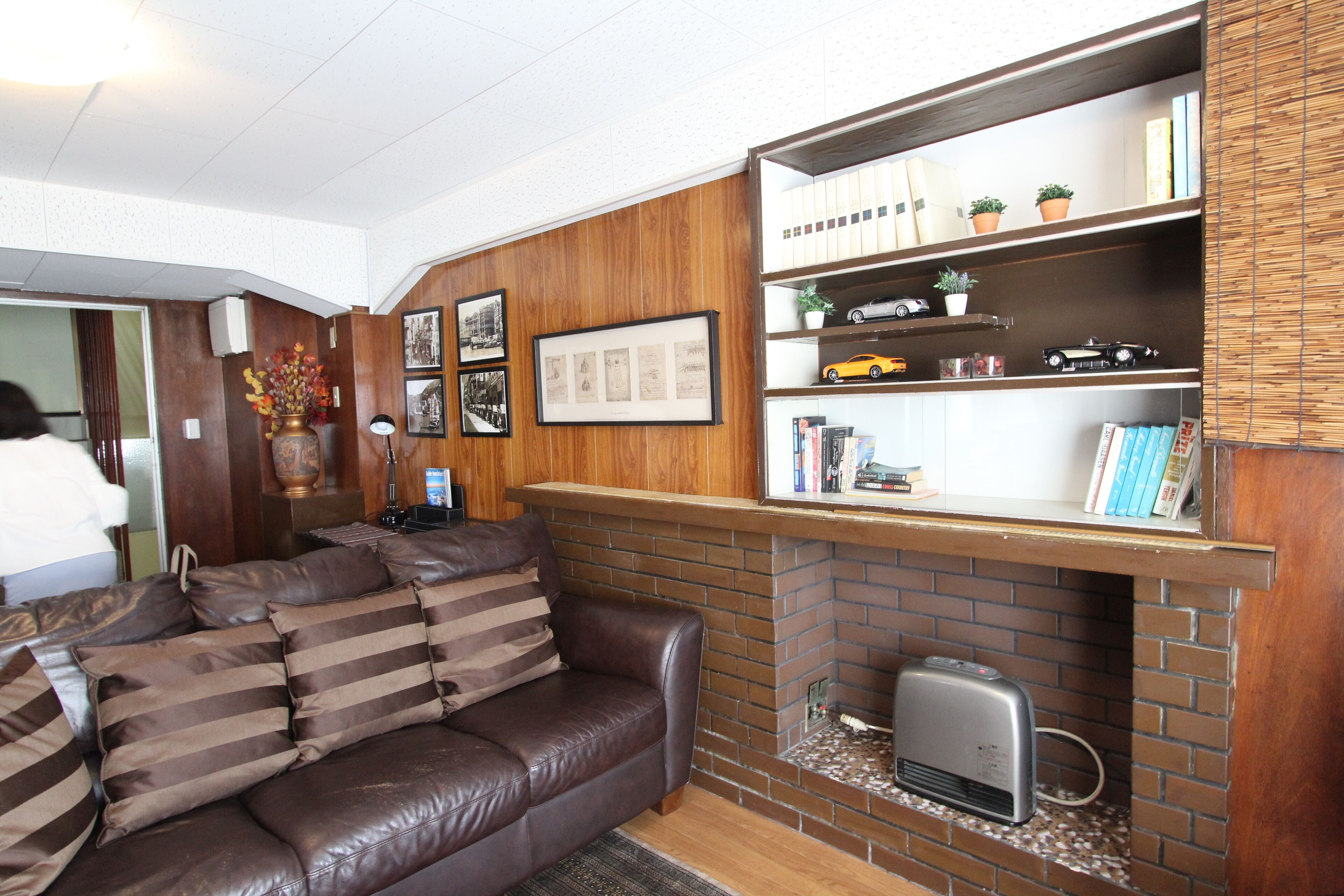 A living room with a brown leather sofa, a brick fireplace, and wooden paneling.