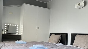 Een moderne slaapkamer met een groot bed, grijze beddengoed, een kaptafel met spiegel en verlichting, en een kledingkast.