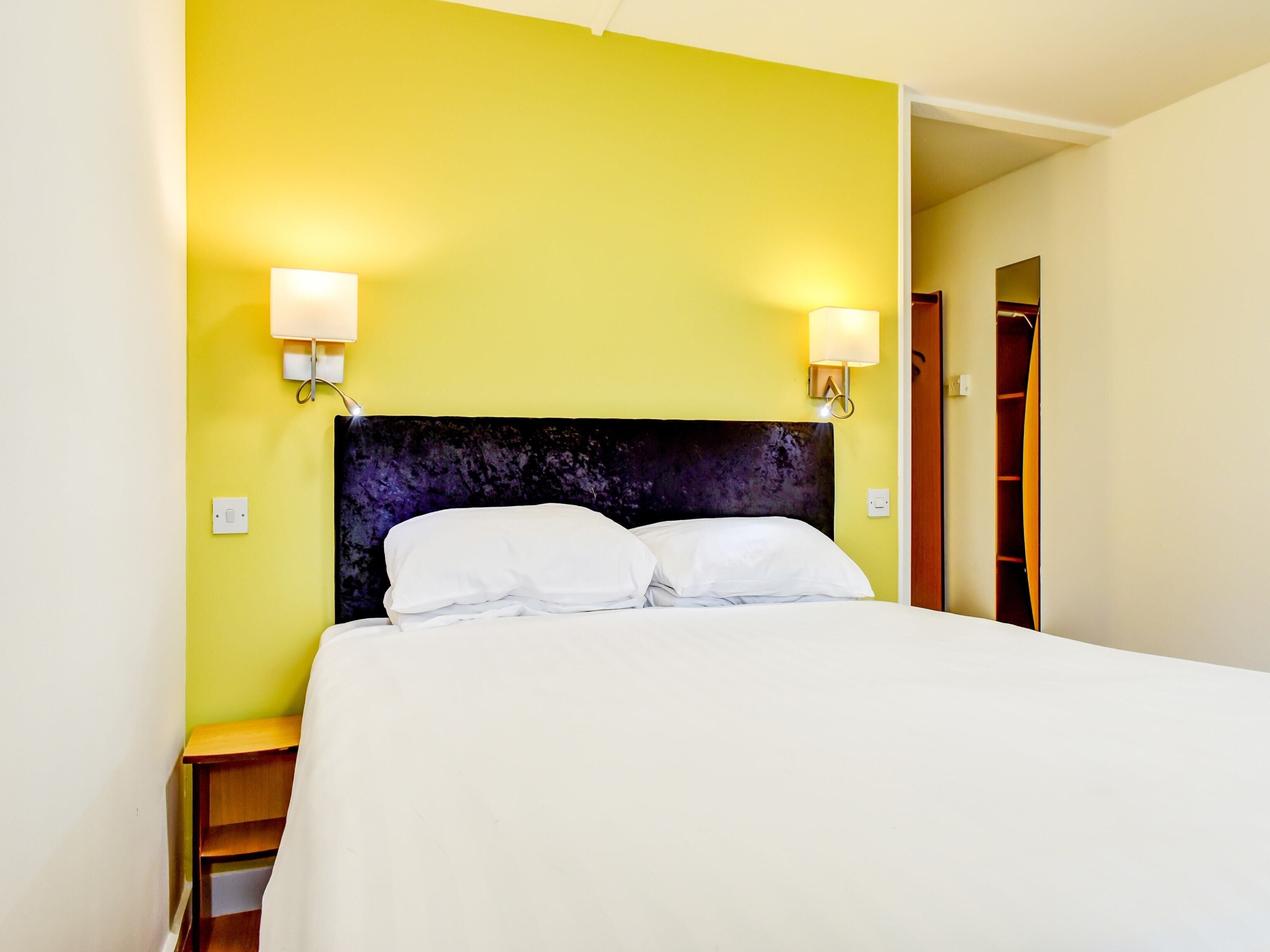A hotel room with a bed, two bedside lamps, a nightstand, and a wooden wardrobe.