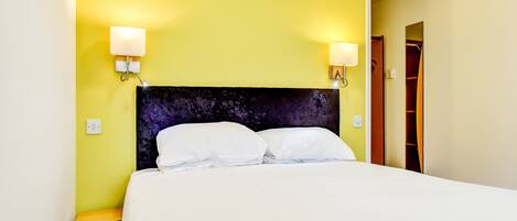 A hotel room with a bed, two bedside lamps, a nightstand, and a wooden wardrobe.