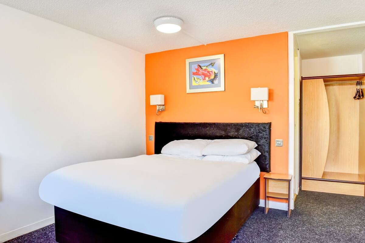 A hotel room with a bed, a small table, two wall-mounted lamps, and a wooden wardrobe.