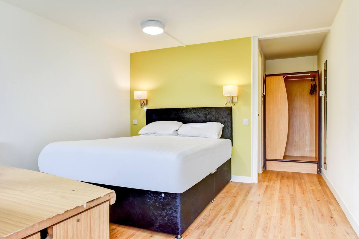 A bedroom with a bed, bedside lamps, a wooden desk, and a walk-in closet.