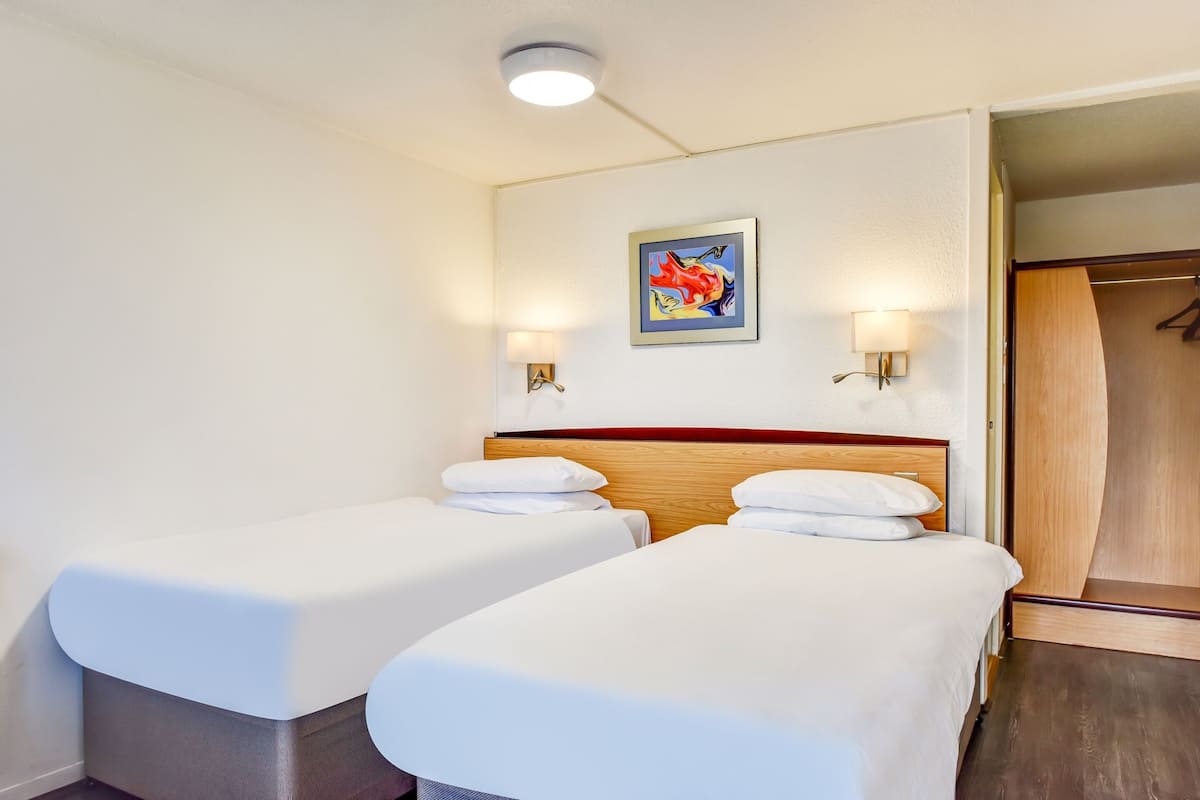 A hotel room with two single beds, a wooden headboard, a painting on the wall, and a wooden wardrobe.