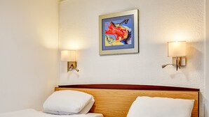 Ett hotellrum med två sängar, en sänggavel i trä och en tavla på väggen.