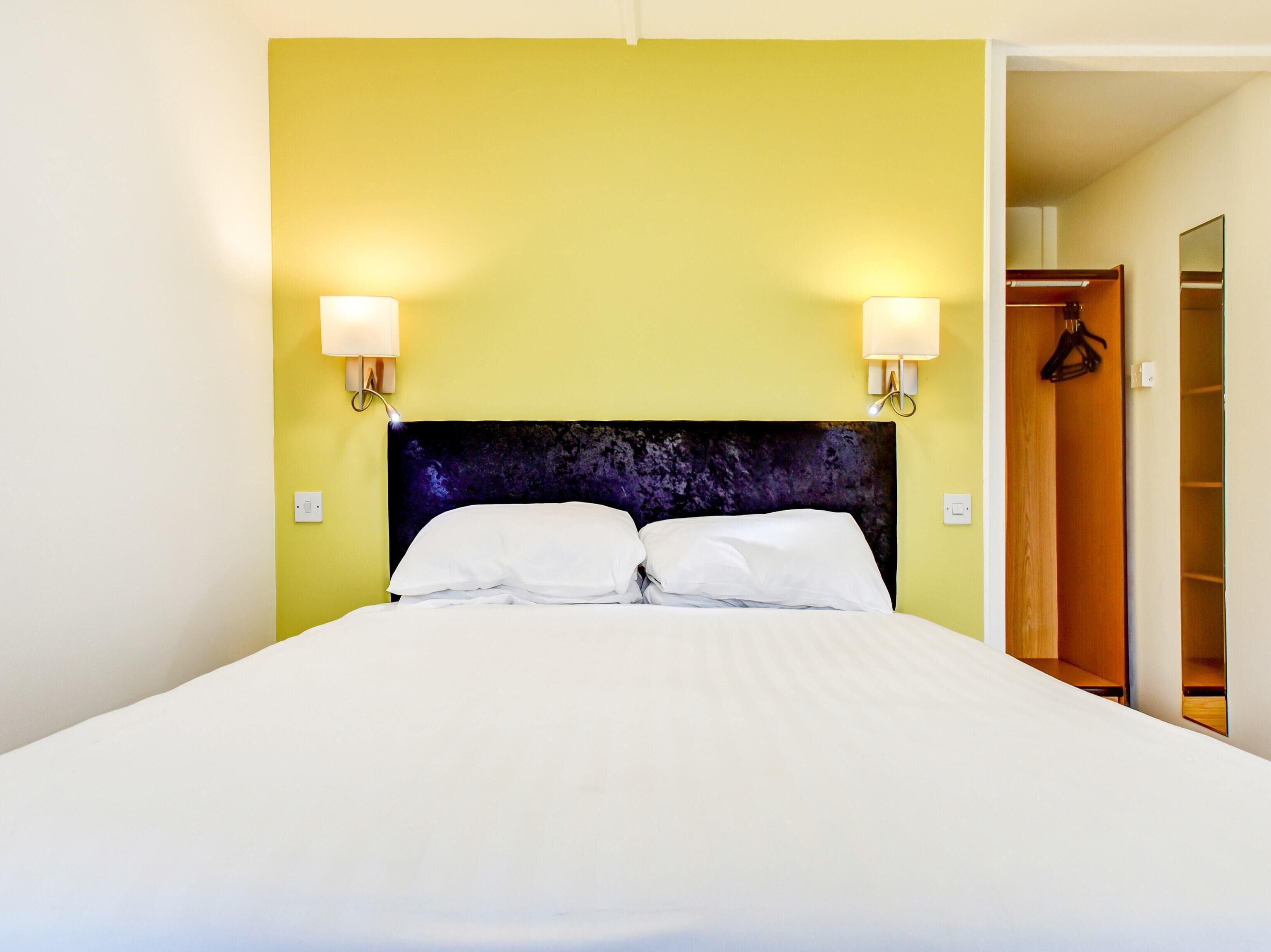 A hotel room with a bed, two wall-mounted lamps, and a wardrobe.
