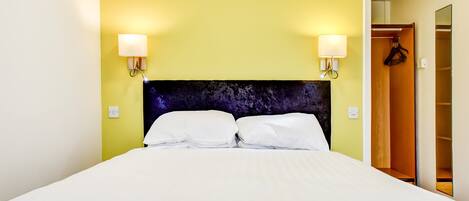 A hotel room with a bed, two wall-mounted lamps, and a wardrobe.
