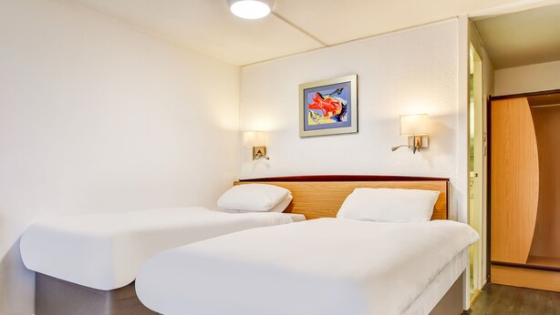 Ett hotellrum med två sängar, en sänggavel i trä, en tavla på väggen och två vägglampor.