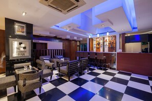 A bar area with checkered flooring, seating, and a bar counter with bottles. - MGM Mark Whitefield (Bengaluru)
