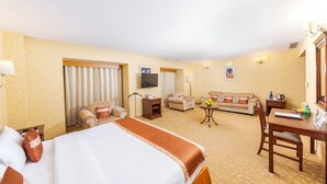 A hotel room with a bed, two armchairs, a sofa, a TV, a desk, and a small table with flowers.
