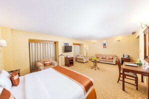 Une chambre d’hôtel avec un lit, deux fauteuils, un canapé, une télévision, un bureau et une petite table agrémentée de fleurs.