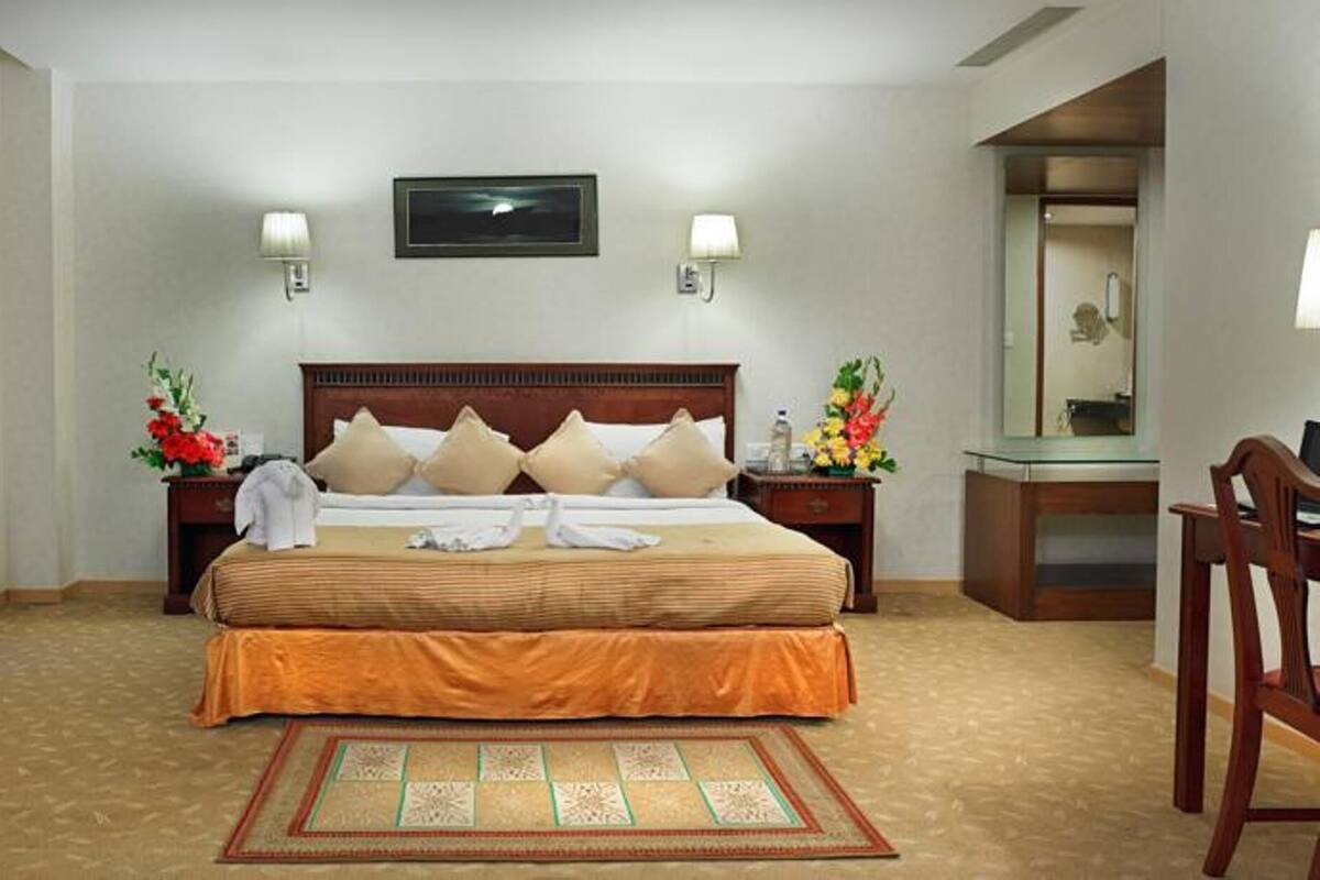 A hotel room with a large bed, two bedside tables, a mirror, a chair, and a coat rack.