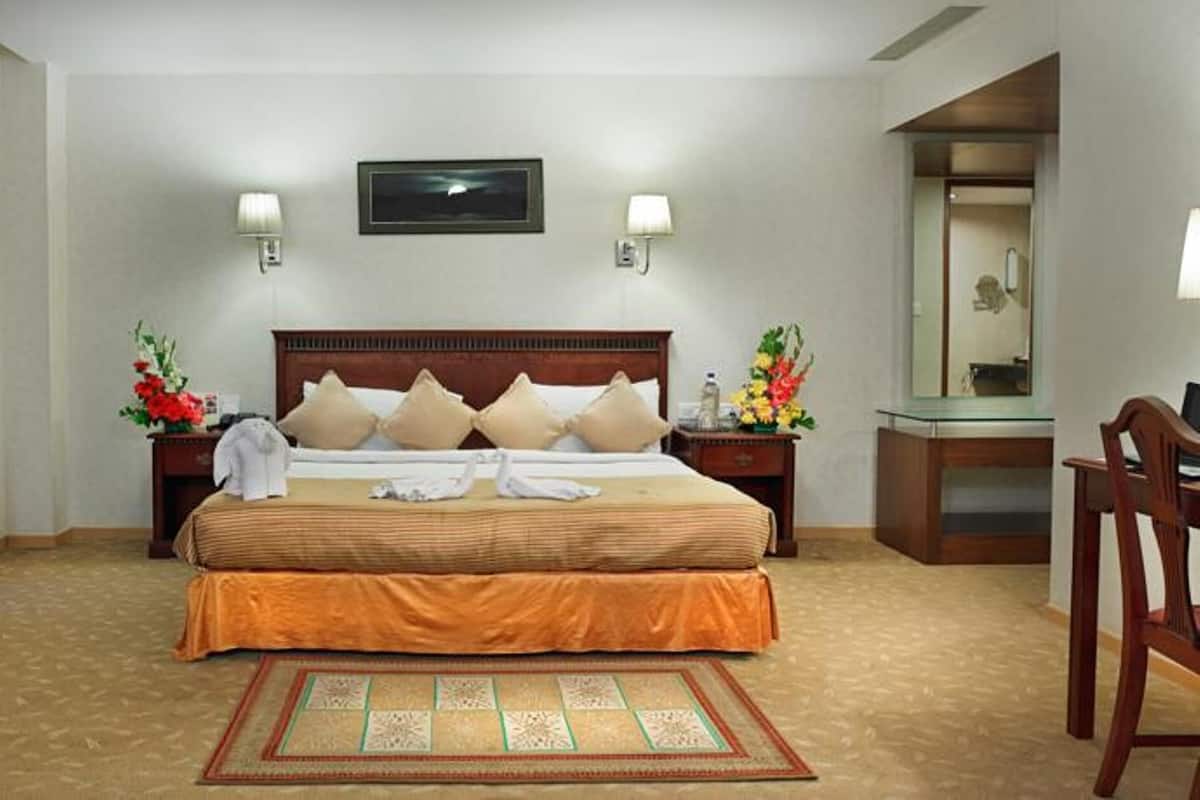 Habitación de hotel con una cama grande, dos mesitas de noche, un espejo, una silla y un perchero.