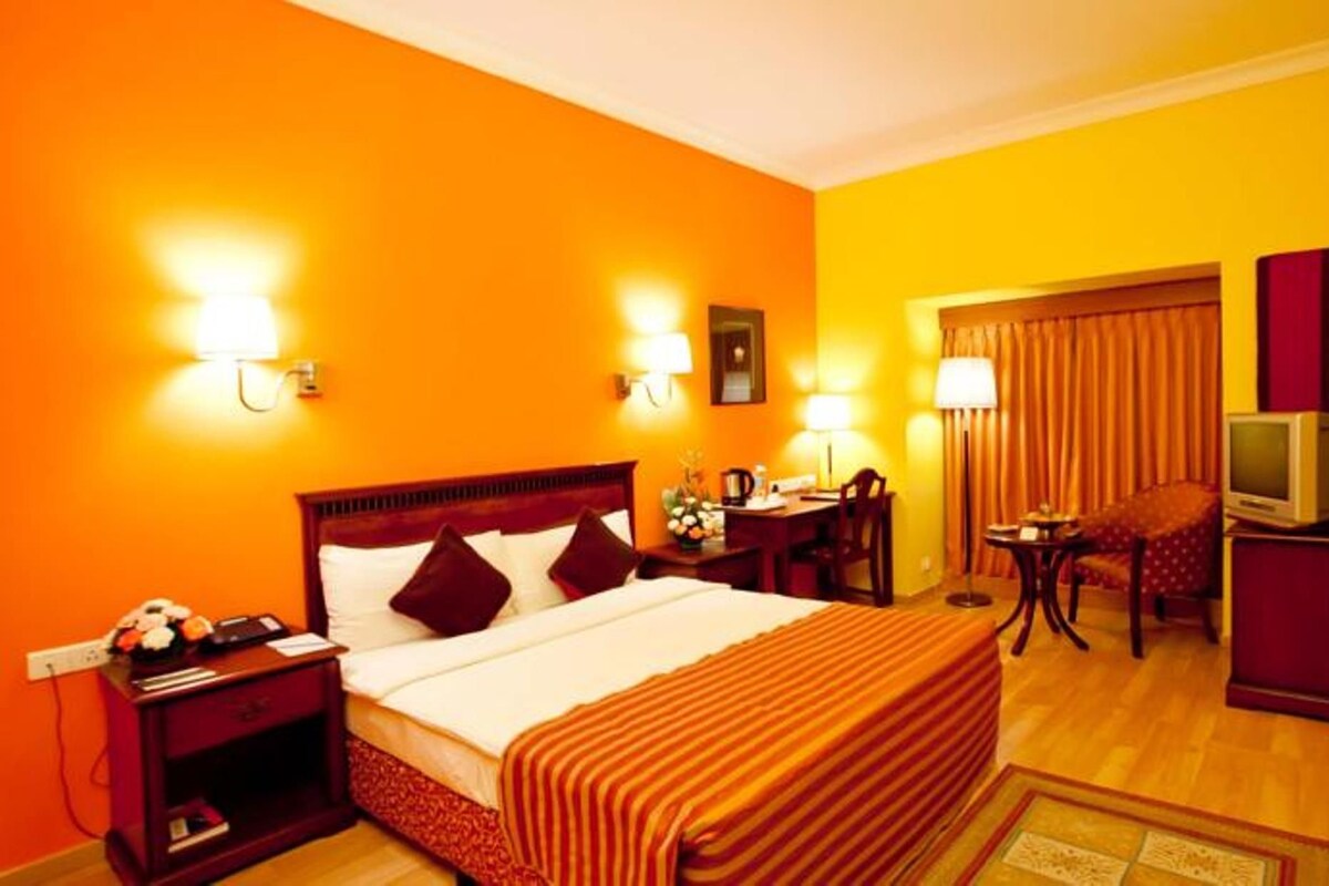 A hotel room with a bed, bedside table, lamp, desk, chair, television, and curtains.