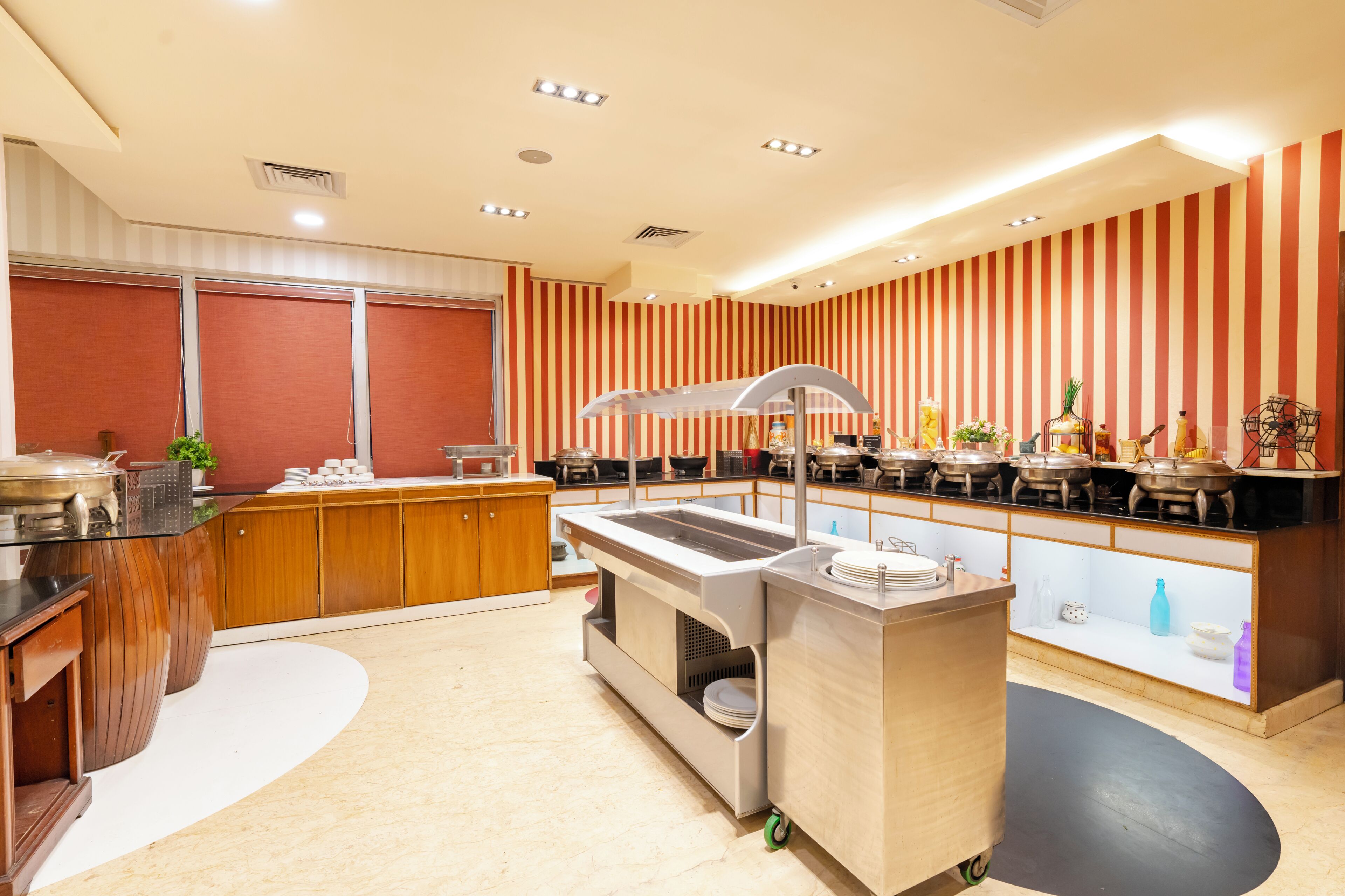 Ein Buffet mit mehreren Servierstationen, einer zentralen Speisenauslage und einer gestreiften Wand im Hintergrund.