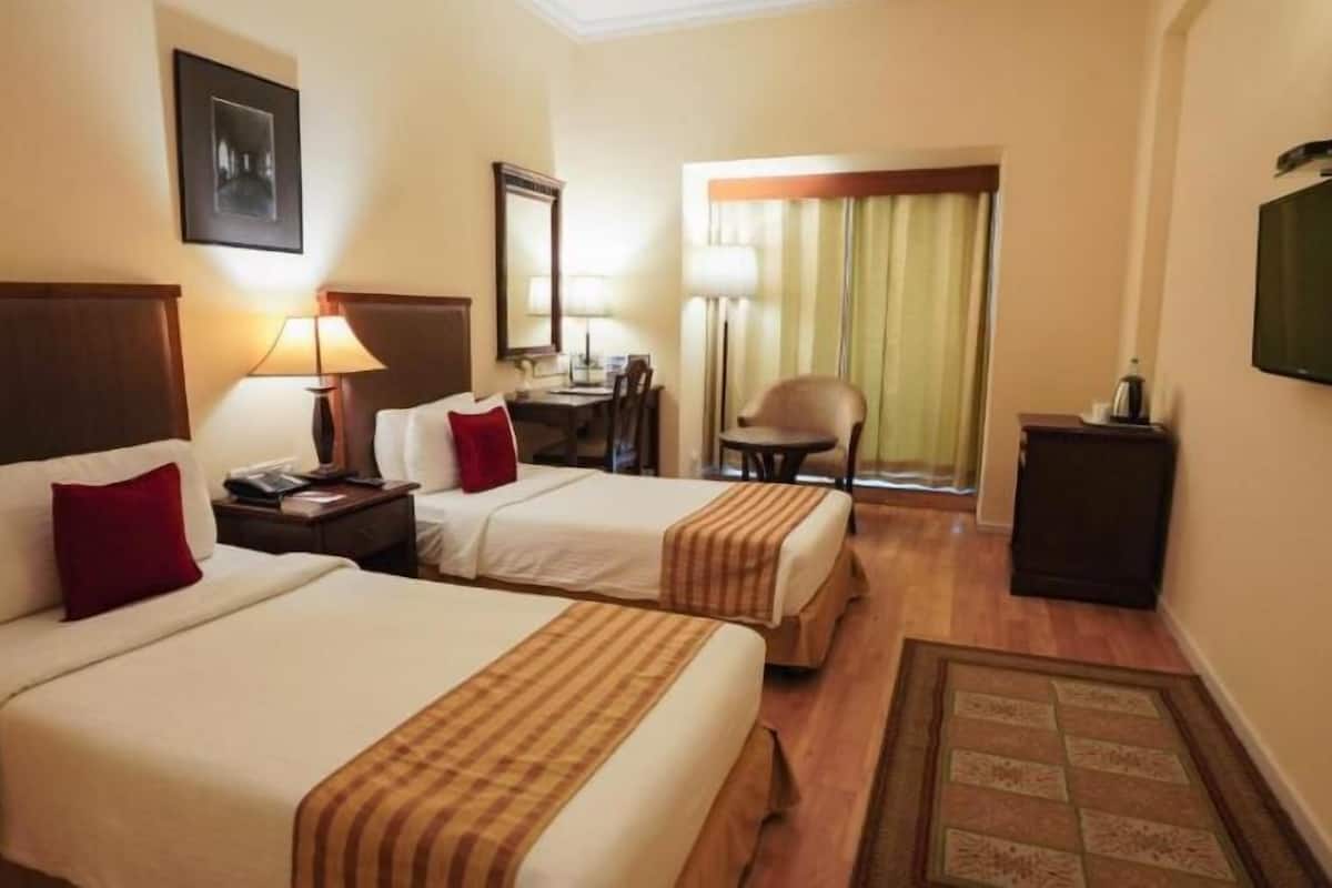 A hotel room with two beds, a desk, a chair, a television, and a window with curtains.