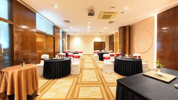 A hotel conference room with multiple round tables, chairs, and a carpeted floor.