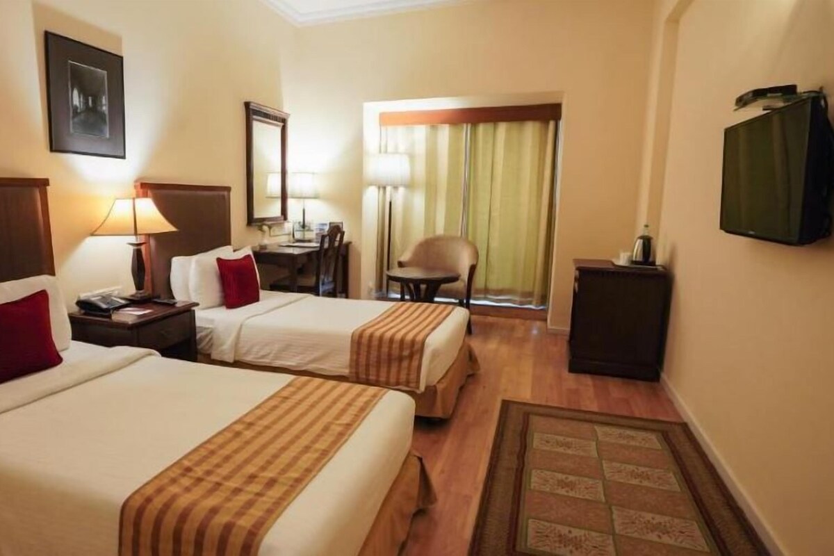 A hotel room with two beds, a desk, a chair, a television, and a window with curtains.