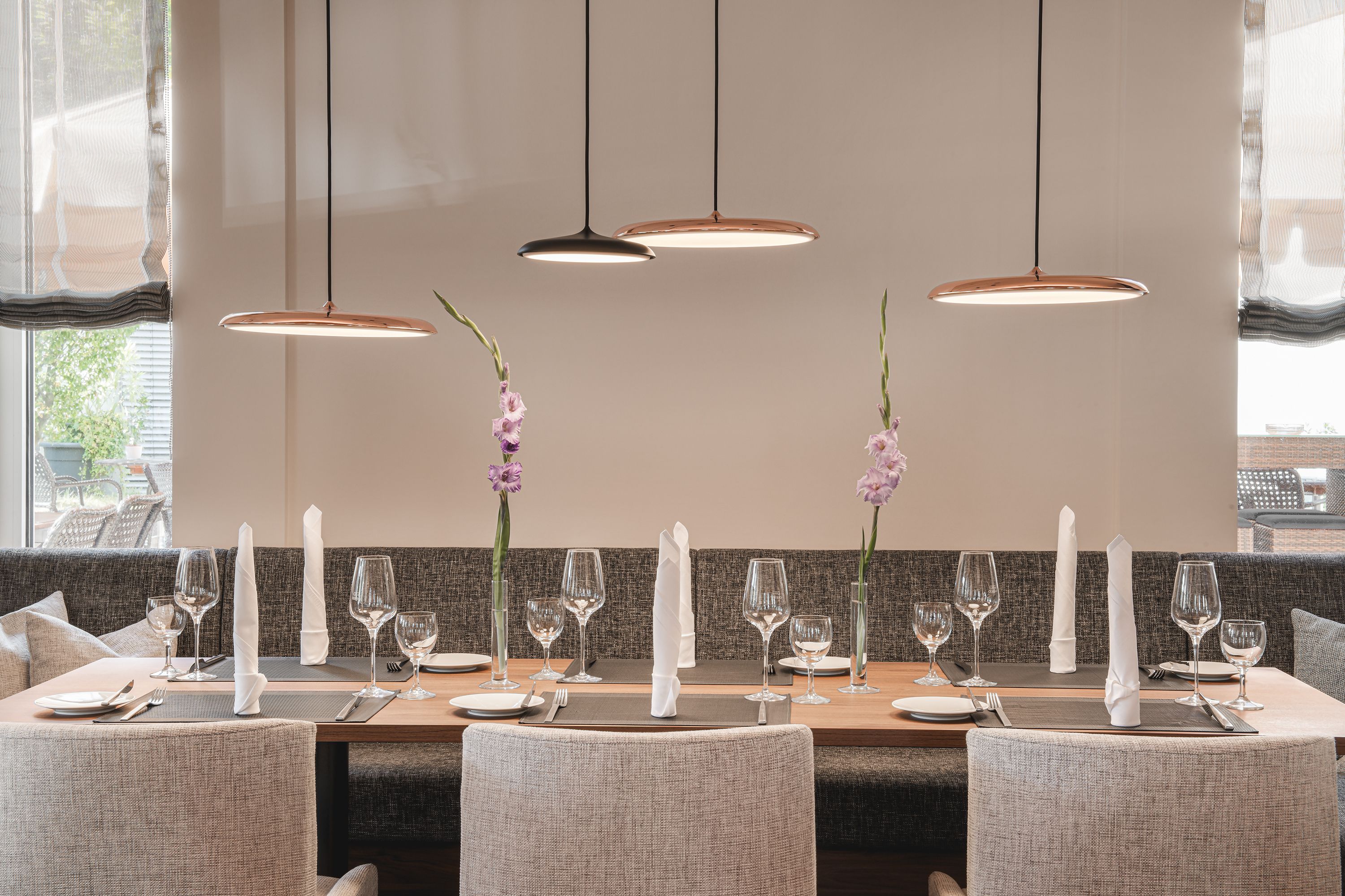 A dining area with a long table set for four, featuring a neutral color palette and modern pendant lighting.