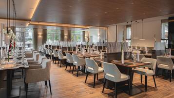 Un restaurant spacieux, doté de nombreuses tables et chaises, de grandes fenêtres et d’un aménagement intérieur moderne.