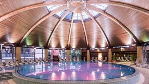 A large indoor swimming pool with a high, arched ceiling and a central skylight.