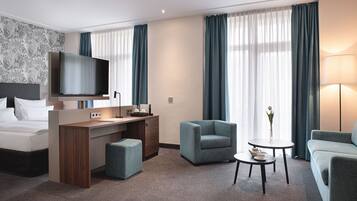 Ein modernes Hotelzimmer mit einem Bett, einem Schreibtisch, einem Fernseher, zwei Sesseln, einem Couchtisch und einer Vase mit einer Blume.