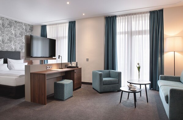 Habitación de hotel moderna con cama, escritorio, televisión, dos sillones, una mesa de centro y un florero con una flor.