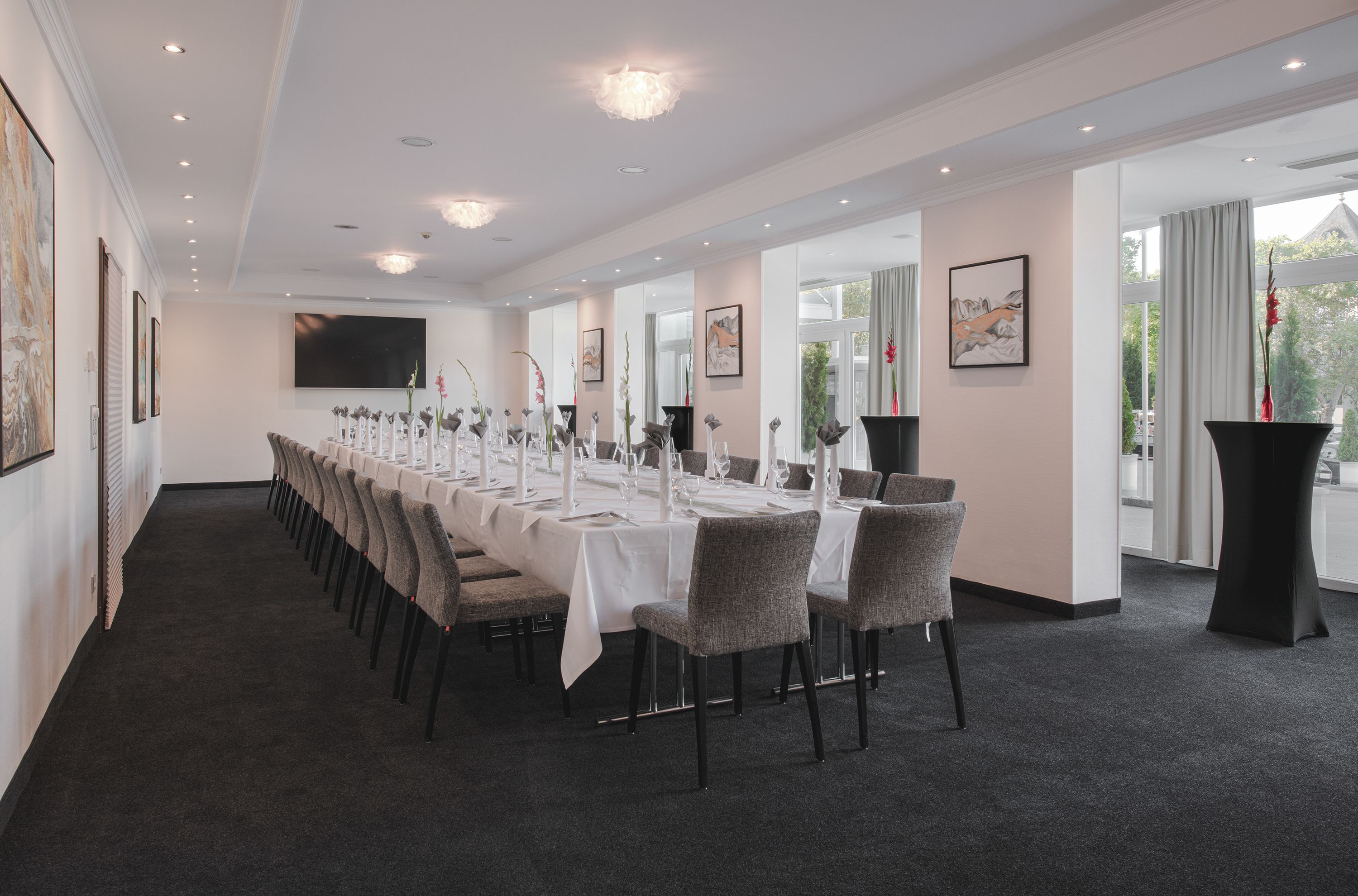 A long conference room with a white tablecloth, grey chairs, and a large screen on the wall.