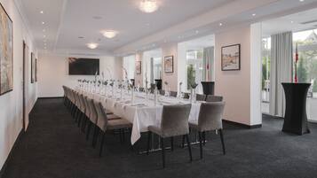 A long conference room with a white tablecloth, grey chairs, and a large screen on the wall.