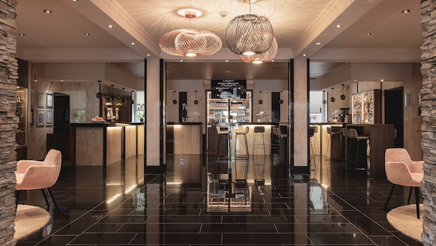 A modern hotel lobby with a polished black floor, two large spherical chandeliers, and a bar area with stools and a counter.